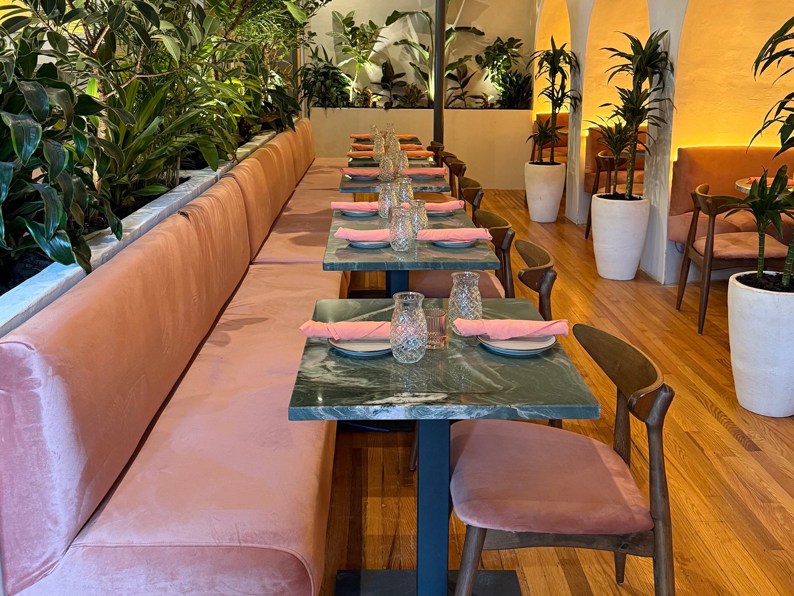 Tropical greenery, pink banquettes, and marble tables inside Aaktun in downtown Clayton