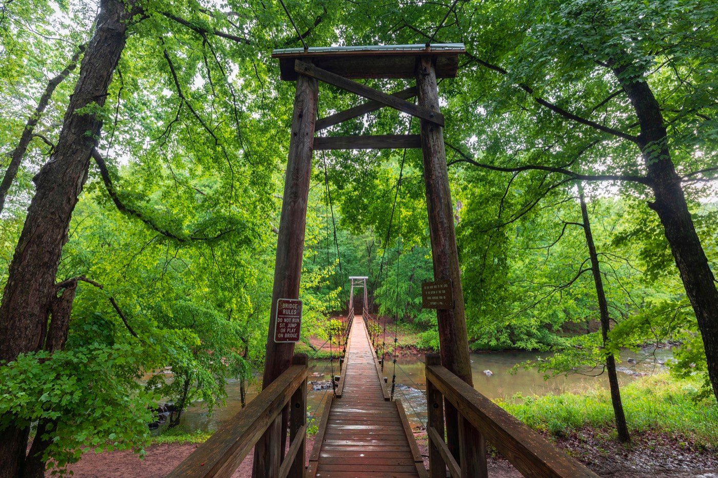 Wooden suspension bridge crossing the Eno River beneath green trees