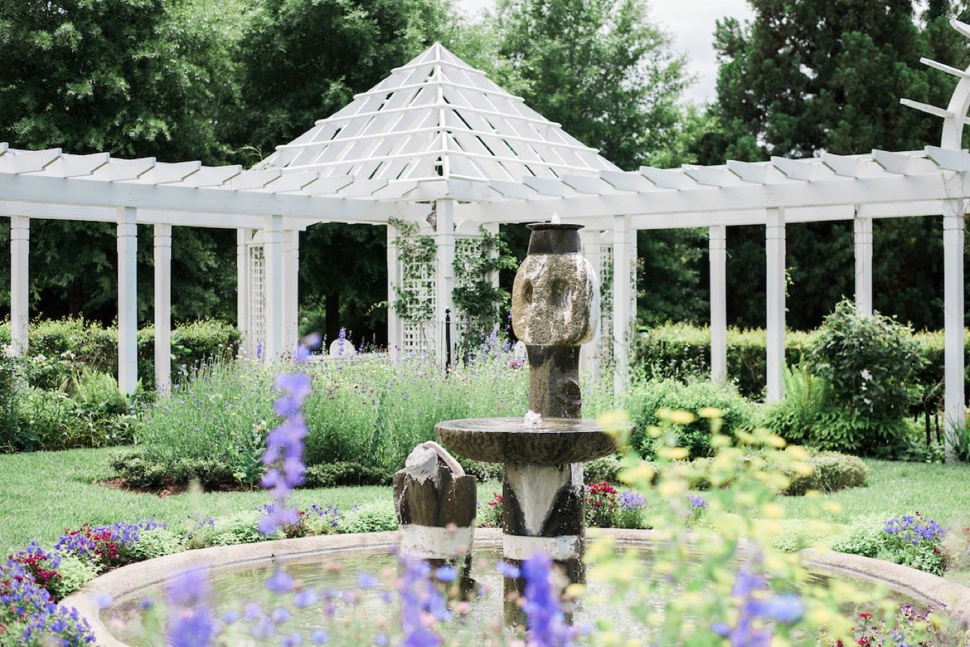 Stone fountain, colorful flowers, and white pergola in the Fearrington Village gardens