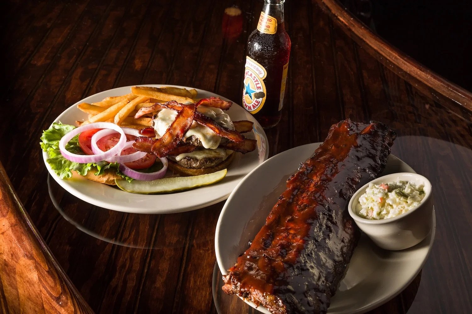 Barbecue ribs, a bacon cheeseburger, fries, coleslaw, and a bottled beer on a wooden table at Manning’s