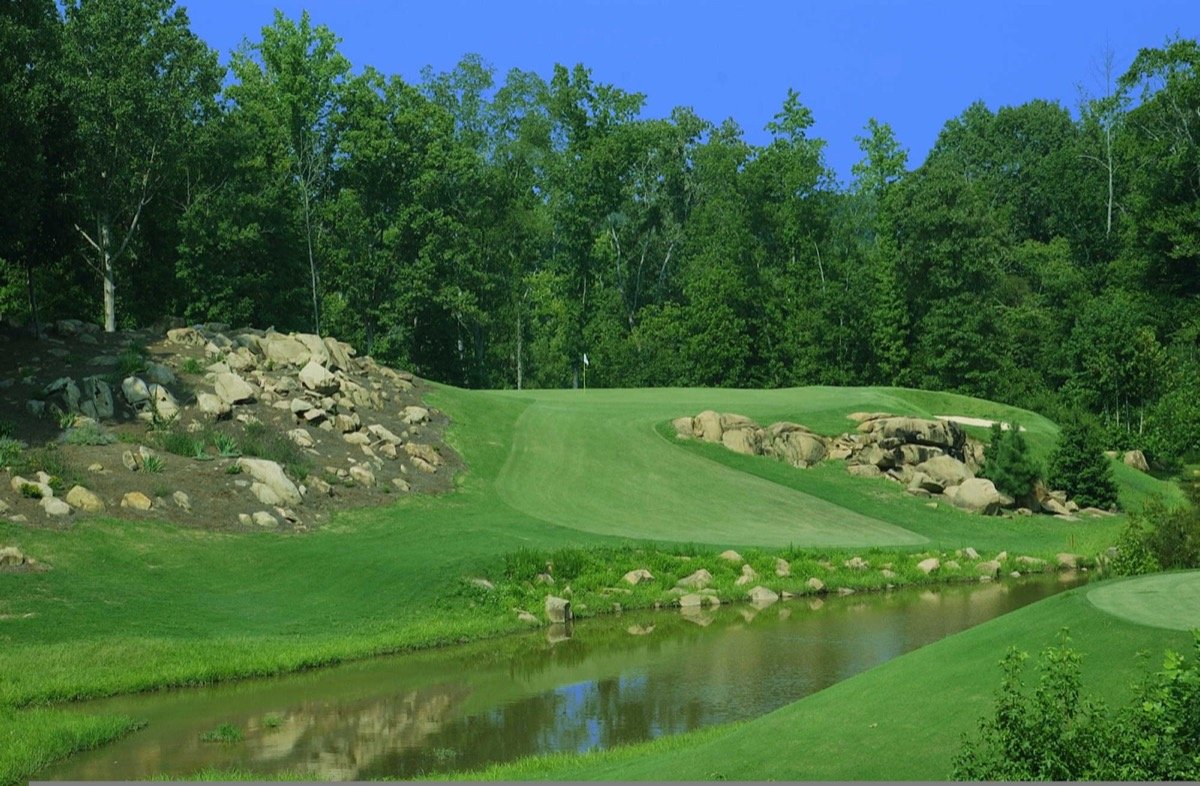 A green framed by rocks, trees, and water at The Neuse Country Club