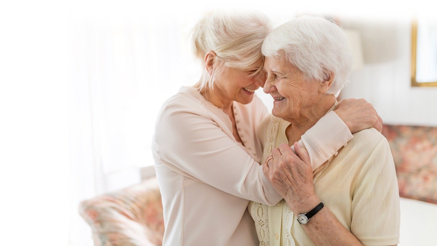 An older woman smiling while embracing an adult family member