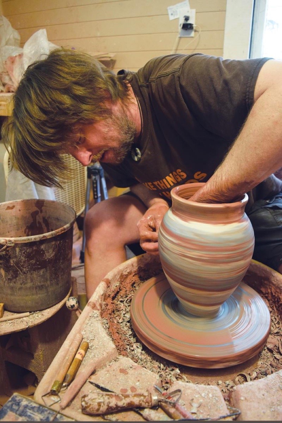 Seagrove potter shaping a tall clay vessel on a wheel