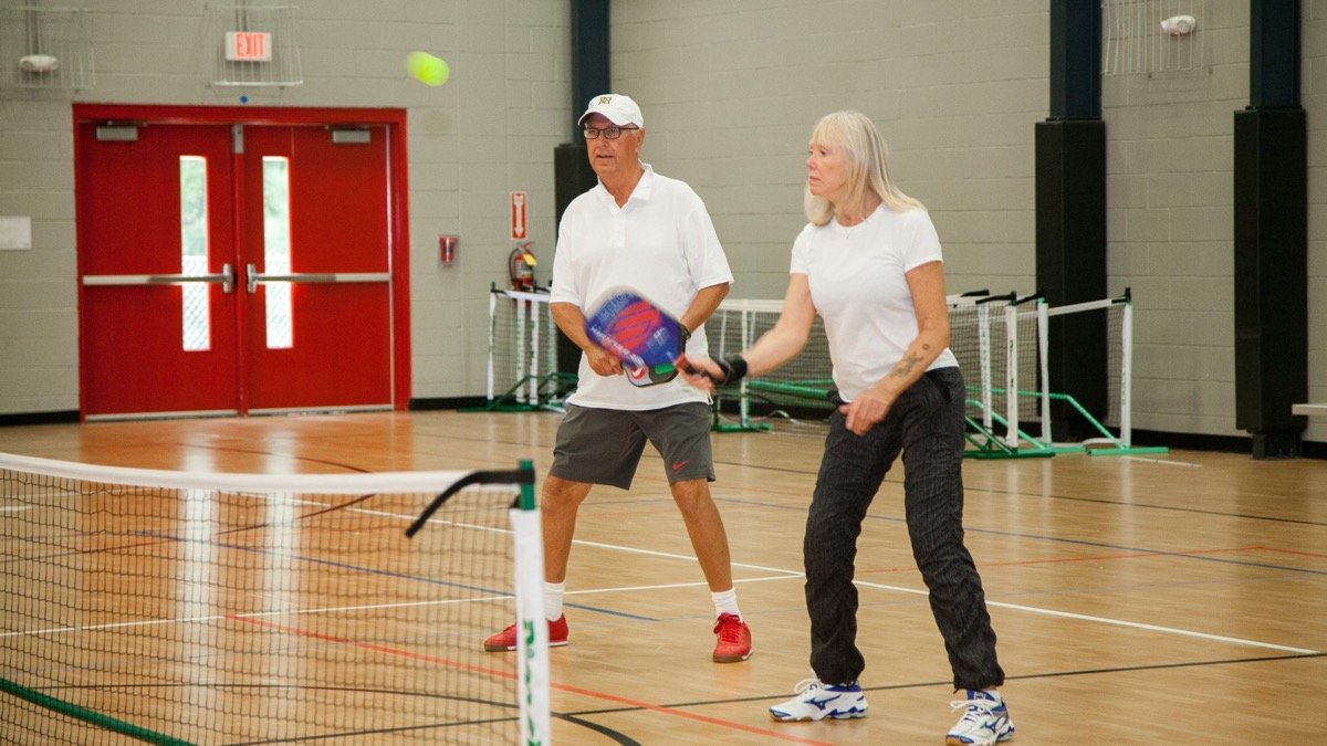 Two older adults playing pickleball indoors at a Raleigh community center