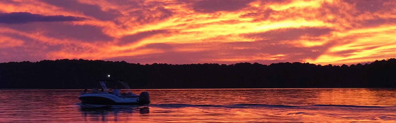 Boat crossing Jordan Lake beneath a colorful sunset sky